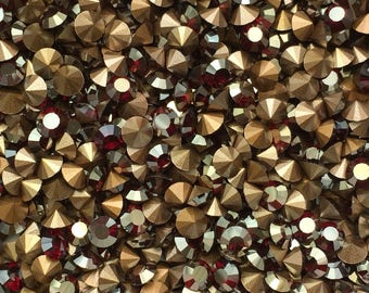 Op de afbeelding: Een close-up van een kom gevuld met kleine, ronde, iriserende strass steentjes. De strass steentjes zijn een mix van goud en rood.