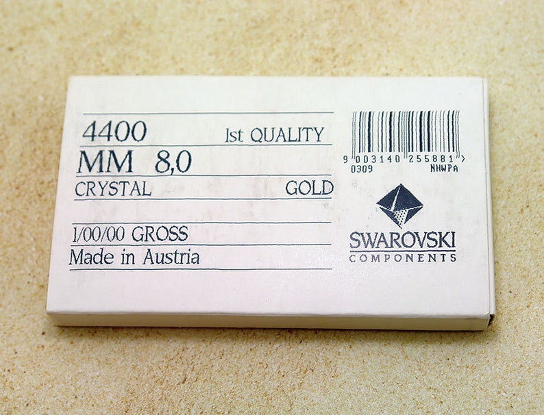 以下が含まれることがあります： 「4400 MM 8,0 CRYSTAL GOLD」と「Made in Austria」を含む黒い文字が書かれた白い箱。箱にはバーコードとスワロフスキーコンポーネンツのロゴも表示されています。