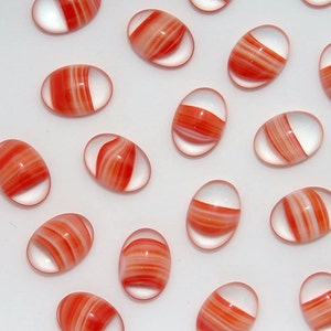 Puede incluir: Cuentas de vidrio ovaladas con un borde transparente y un llamativo diseño a rayas rojas y blancas. Estas cuentas decorativas están dispersas sobre una superficie blanca, mostrando sus diseños únicos y coloridos. Ideales para manualidades y joyería.