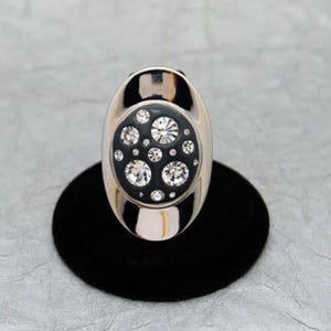 May include: A silver ring with a black enamel setting featuring a cluster of clear rhinestones.