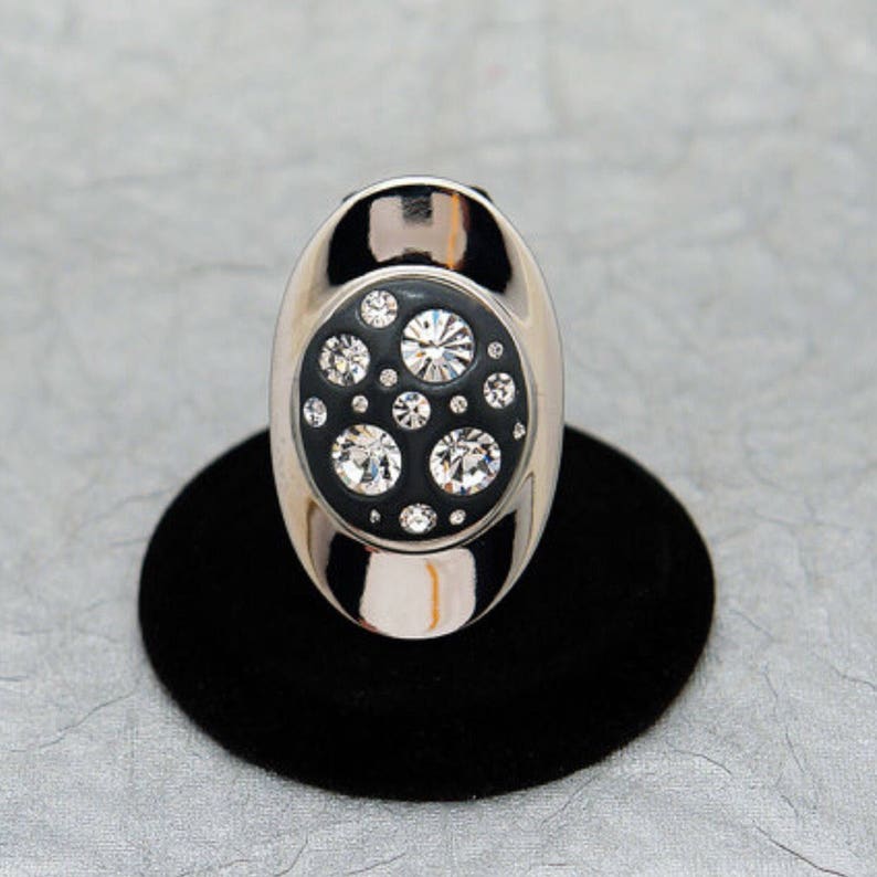 May include: A silver ring with a black enamel setting featuring a cluster of clear rhinestones.