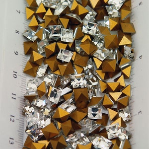 May include: A mix of gold and clear glass pyramid and square shaped rhinestones.