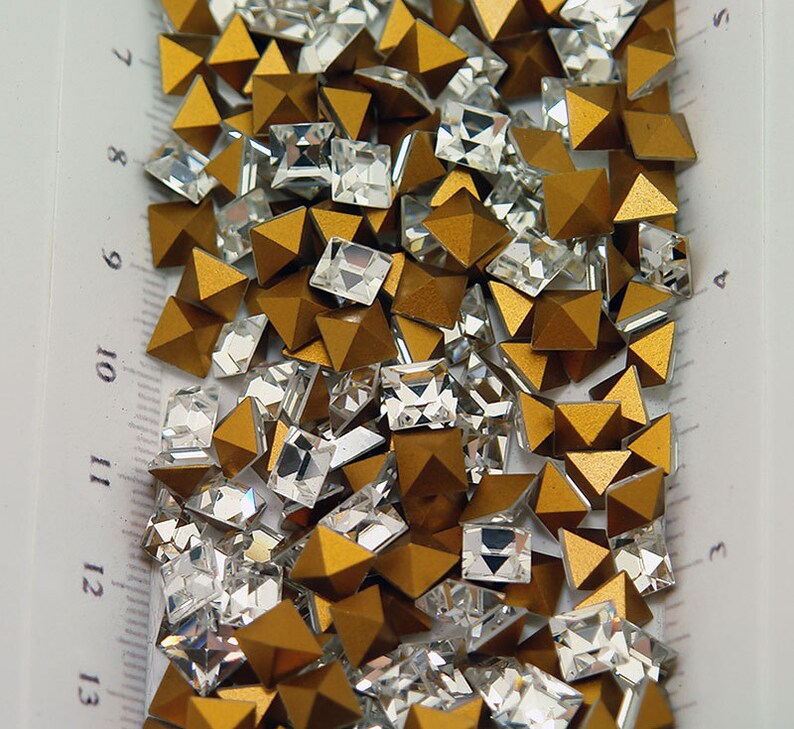 May include: A mix of gold and clear glass pyramid and square shaped rhinestones.