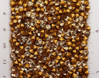 May include: Close-up of a collection of golden-brown rhinestones. The rhinestones are faceted, reflecting light, and are of varying sizes. The image is a top-down view, showcasing the texture and sparkle of the gemstones. Ideal for jewelry making and craft projects.