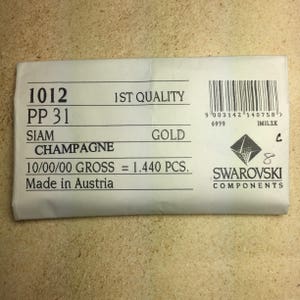 May include: A white paper bag with the text "1012 PP 31 SIAM CHAMPAGNE 1ST QUALITY GOLD 10/00/00 GROSS = 1.440 PCS. Made in Austria" and a black and white logo that says "SWAROVSKI COMPONENTS".