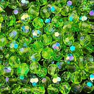 Puede incluir: Primer plano de un mont&oacute;n de cuentas facetadas de color verde lima. Las cuentas tienen m&uacute;ltiples facetas que capturan la luz, creando un efecto brillante. Las cuentas son redondas con un agujero en el centro para ensartar.