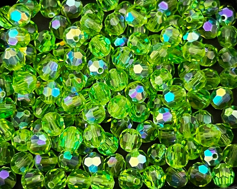 Puede incluir: Primer plano de un mont&oacute;n de cuentas facetadas de color verde lima. Las cuentas tienen m&uacute;ltiples facetas que capturan la luz, creando un efecto brillante. Las cuentas son redondas con un agujero en el centro para ensartar.