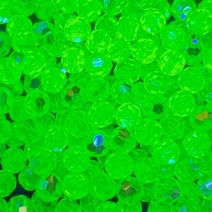 Puede incluir: Primer plano de un mont&oacute;n de cuentas facetadas de color verde ne&oacute;n. Las cuentas son redondas con m&uacute;ltiples facetas que capturan la luz, creando un efecto brillante. Las cuentas est&aacute;n dispersas, llenando el marco.