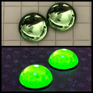 May include: Two green glass cabochons, one with a reflective surface and the other with a fluorescent green glow.