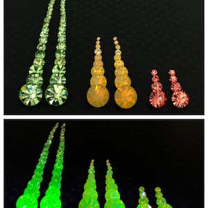 May include: A set of earrings with green, orange, and red crystals. The earrings are in different sizes and shapes, and they are all made of glass. The earrings are arranged in a row on a black background.