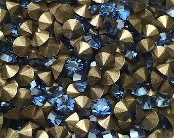 May include: Close-up of a collection of blue and bronze-colored rhinestones. The rhinestones are a mix of round and pointed shapes, with a faceted design that catches the light. The bronze rhinestones have a metallic finish.