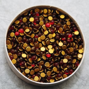 May include: A white bowl filled with a mixture of small, round, gold and red beads.