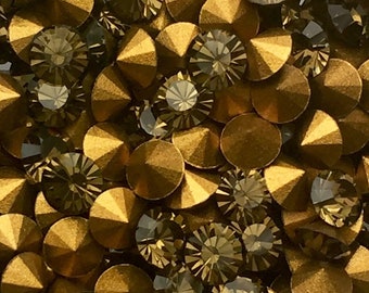 May include: Close-up of a collection of golden-brown and smoky-gray rhinestones. The rhinestones have a faceted, cone-like shape, reflecting light. The arrangement is dense, creating a sparkling, textured surface. Ideal for craft projects.