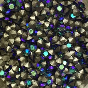 Puede incluir: Primer plano de una colección de pedrería iridiscente. La pedrería es de color gris oscuro con facetas que reflejan tonos de azul, verde y morado. Las gemas son redondas y tienen la parte posterior plana.