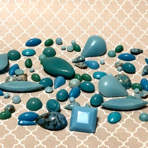 Puede incluir: Una colección de cuentas de piedras preciosas azules y verdes de varias formas y tamaños. Las cuentas incluyen formas redondas, ovaladas, de lágrima y cuadradas, con una mezcla de texturas sólidas y estampadas. El fondo es una superficie clara beige estampada.