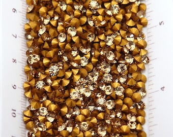 May include: Close-up of a collection of golden-colored rhinestones. The rhinestones are arranged closely together, with a mix of faceted and rounded shapes. The overall effect is a sparkling, textured surface, ideal for craft projects.
