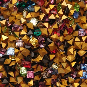 May include: A large assortment of gold pyramid-shaped studs with various colored square rhinestones. The rhinestones are in shades of red, green, blue, purple, and black.