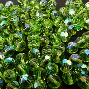 Puede incluir: Un conjunto de cuentas facetadas de color verde claro con reflejos iridiscentes. Estas peque&ntilde;as cuentas decorativas est&aacute;n dispersas, mostrando sus m&uacute;ltiples facetas y la refracci&oacute;n de la luz. Ideal para la fabricaci&oacute;n de joyas y manualidades.