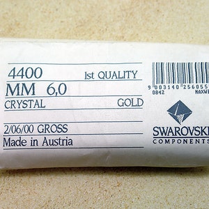 May include: A white label with black text that reads "4400 MM 6,0 CRYSTAL 2/06/00 GROSS Made in Austria 1st QUALITY GOLD" and a barcode with the text "9 003140 256055> 0842 NAXWP" and a Swarovski logo with the text "SWAROVSKI COMPONENTS".