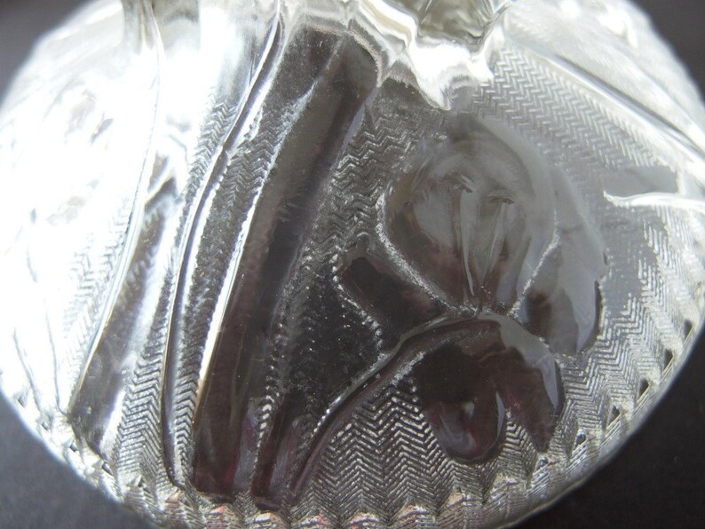 May include: A clear glass lid with a textured design featuring a flower pattern. The lid has a raised edge and a smooth, polished surface.