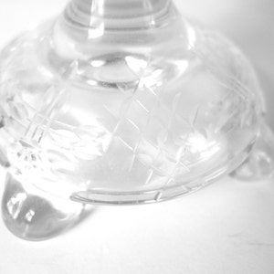May include: A clear glass pedestal with a decorative etched pattern and three feet.