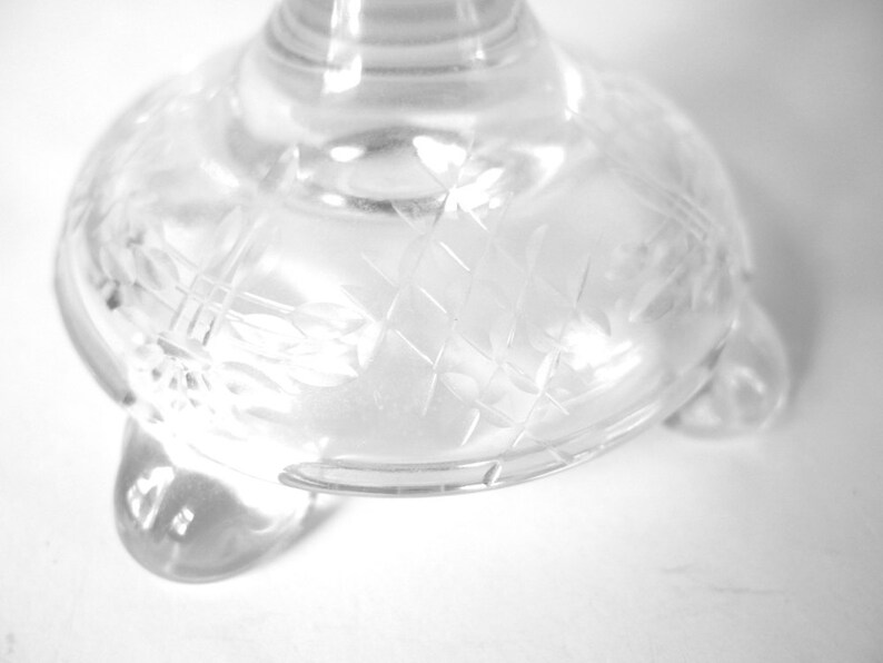 May include: A clear glass pedestal with a decorative etched pattern and three feet.