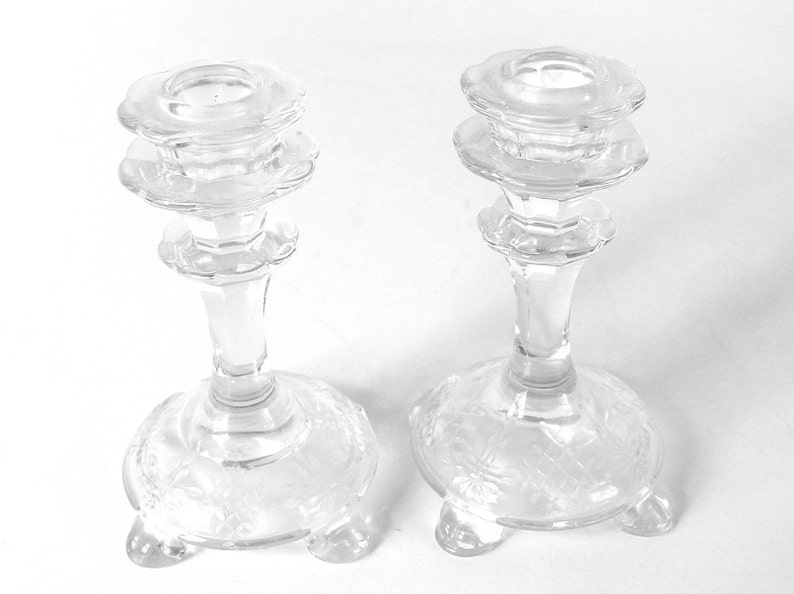 May include: Two clear glass candle holders with a scalloped design and three feet. The candle holders are made of crystal and have a delicate, elegant look.
