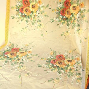 May include: A beige tablecloth with a yellow lace border features a floral pattern of yellow, orange, and red flowers. The flowers are arranged in bouquets and are scattered across the tablecloth.
