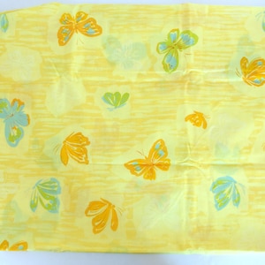 May include: Yellow fabric featuring a repeating butterfly pattern in orange, blue, and green. The butterflies are set against a textured, striped background. The fabric is folded.