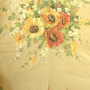 May include: A beige fabric with a floral print featuring yellow, red, and white flowers. The fabric has a yellow and white lace trim on the right side.