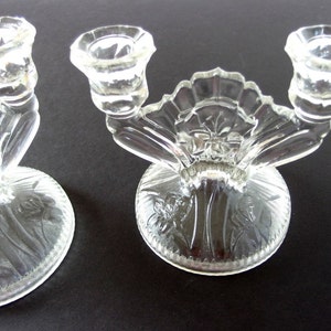 May include: Two clear glass candle holders with a floral design. Each holder has three candle cups and a round base.