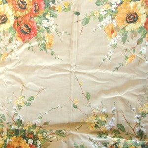 May include: A beige tablecloth with a floral pattern featuring yellow, orange, and white flowers. The flowers are arranged in a repeating pattern across the fabric.