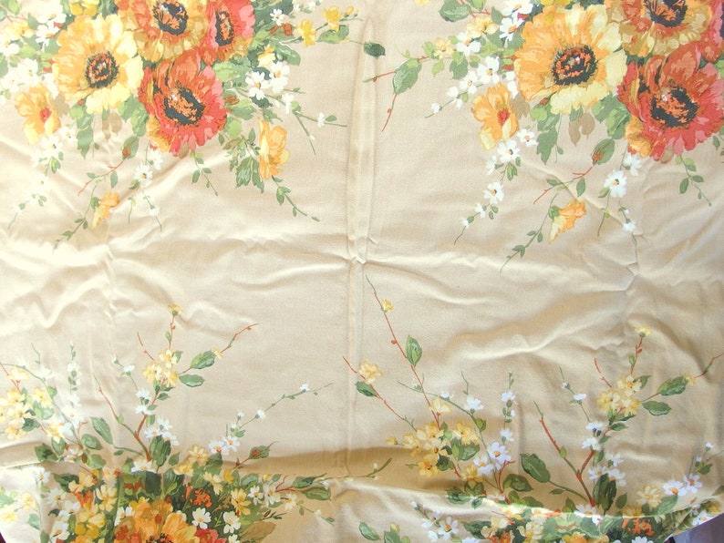 May include: A beige tablecloth with a floral pattern featuring yellow, orange, and white flowers. The flowers are arranged in a repeating pattern across the fabric.