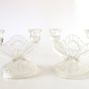 May include: A pair of clear glass candle holders with a floral design. Each holder has three candle cups and a decorative base.