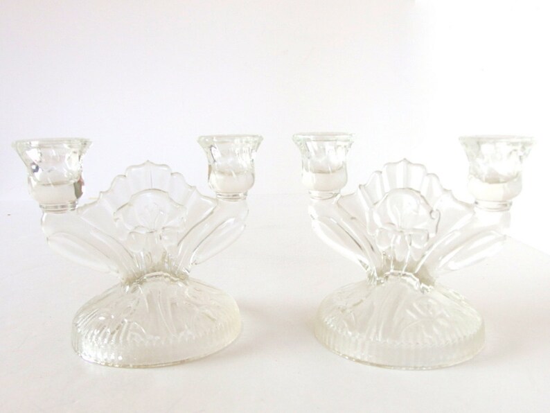 May include: A pair of clear glass candle holders with a floral design. Each holder has three candle cups and a decorative base.