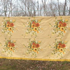 May include: A beige tablecloth with a floral pattern featuring yellow, orange, and white flowers. The tablecloth has a yellow fringe border.
