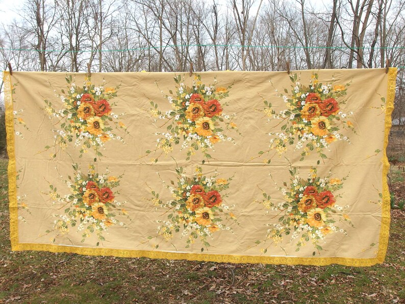 May include: A beige tablecloth with a floral pattern featuring yellow, orange, and white flowers. The tablecloth has a yellow fringe border.