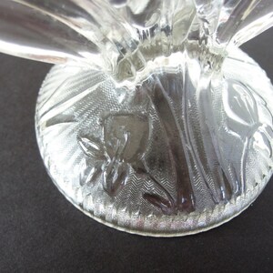 May include: Clear glass pedestal with a floral design etched into the base. The base is round and has a scalloped edge.