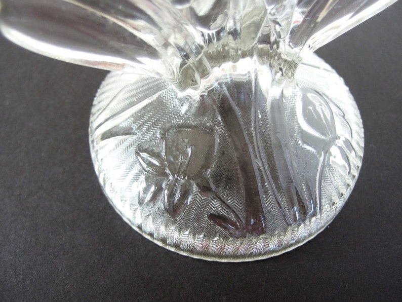 May include: Clear glass pedestal with a floral design etched into the base. The base is round and has a scalloped edge.