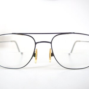 May include: Black metal frame eyeglasses with clear lenses. The glasses have a thin metal bridge and gold-colored nose pads.
