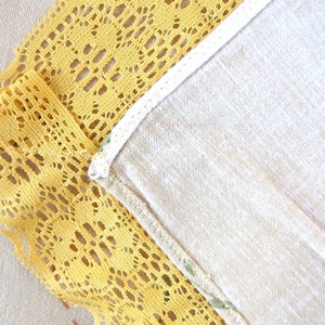 May include: A close-up of a yellow lace trim sewn to a white fabric. The lace has a delicate floral pattern.