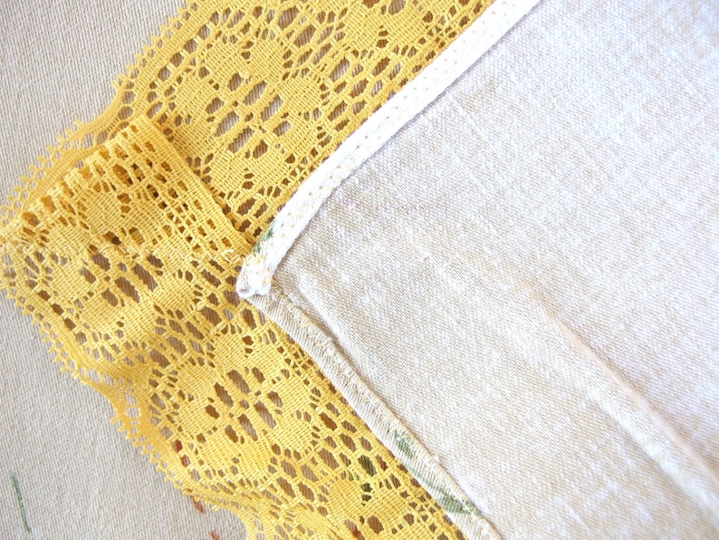 May include: A close-up of a yellow lace trim sewn to a white fabric. The lace has a delicate floral pattern.