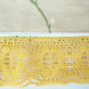 May include: A close-up of a yellow lace trim with a delicate floral pattern. The lace is sewn onto a beige fabric with a floral print.