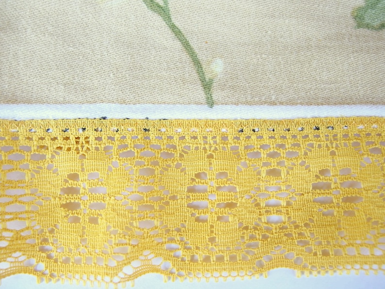 May include: A close-up of a yellow lace trim with a delicate floral pattern. The lace is sewn onto a beige fabric with a floral print.