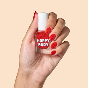 May include: A red nail polish bottle with a clear glass bottle and a white cap. The bottle has the words "HAPPY RUDY" printed on the label. The bottle is being held by a hand with red glitter nail polish.