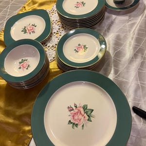 Puede incluir: Un juego de vajilla vintage con platos, cuencos y tazas de té. El juego tiene un centro color crema con un diseño de rosa rosa y un borde verde. Los bordes están adornados con dorado. El juego incluye platos y cuencos de varios tamaños.