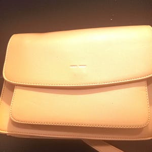 May include: A light brown leather crossbody bag with a flap closure and a small logo on the front.