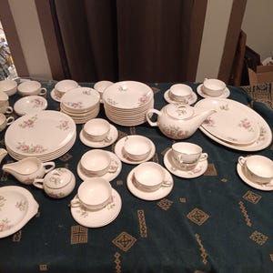 Può includere: Un set da tè floreale vintage con teiera, lattiera, zuccheriera, tazze, piattini e piatti. Il set presenta un delicato motivo floreale in tonalità rosa e verde su sfondo bianco.