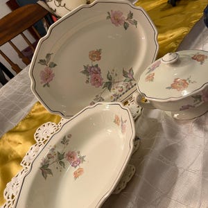 Può includere: Un set da portata in porcellana di tre pezzi con un motivo floreale di fiori rosa, arancioni e viola. Il set comprende un piatto ovale, una zuppiera con coperchio e un piatto da portata più piccolo, tutti con bordi smerlati.