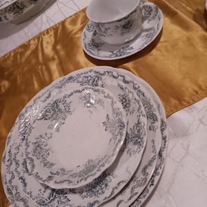 May include: A set of three white ceramic plates with a blue and gray floral pattern. The plates are stacked on top of each other, with the largest plate on the bottom and the smallest plate on top.